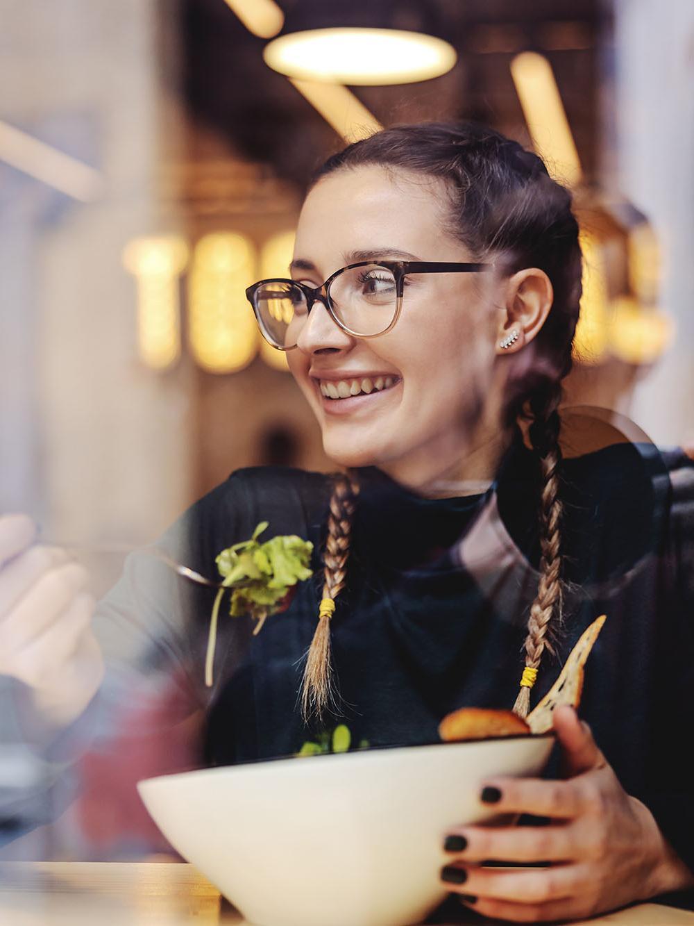 Smiling student eating a healthy meal in a café, representing the Nutrition BSc (Hons) degree at the University of Chester focused on food, health, and wellbeing.
