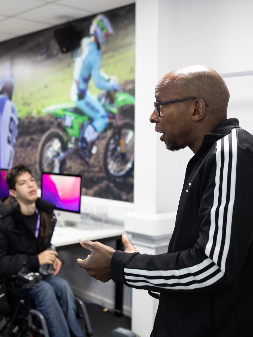 Sports Journalism BA (Hons) class at the University of Chester, showing a lecturer presenting to students in a modern computer lab with sports-themed wall graphics.