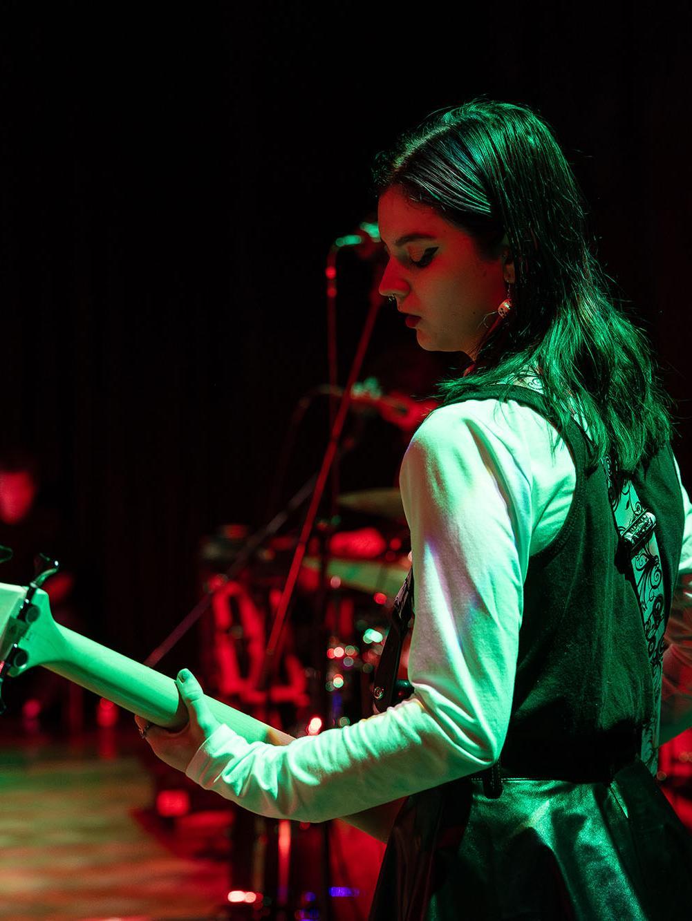 Students performing live on stage with electric guitars and drums under vibrant red and green lighting, showcasing practical skills developed on the Popular Music Performance BA (Hons) course.