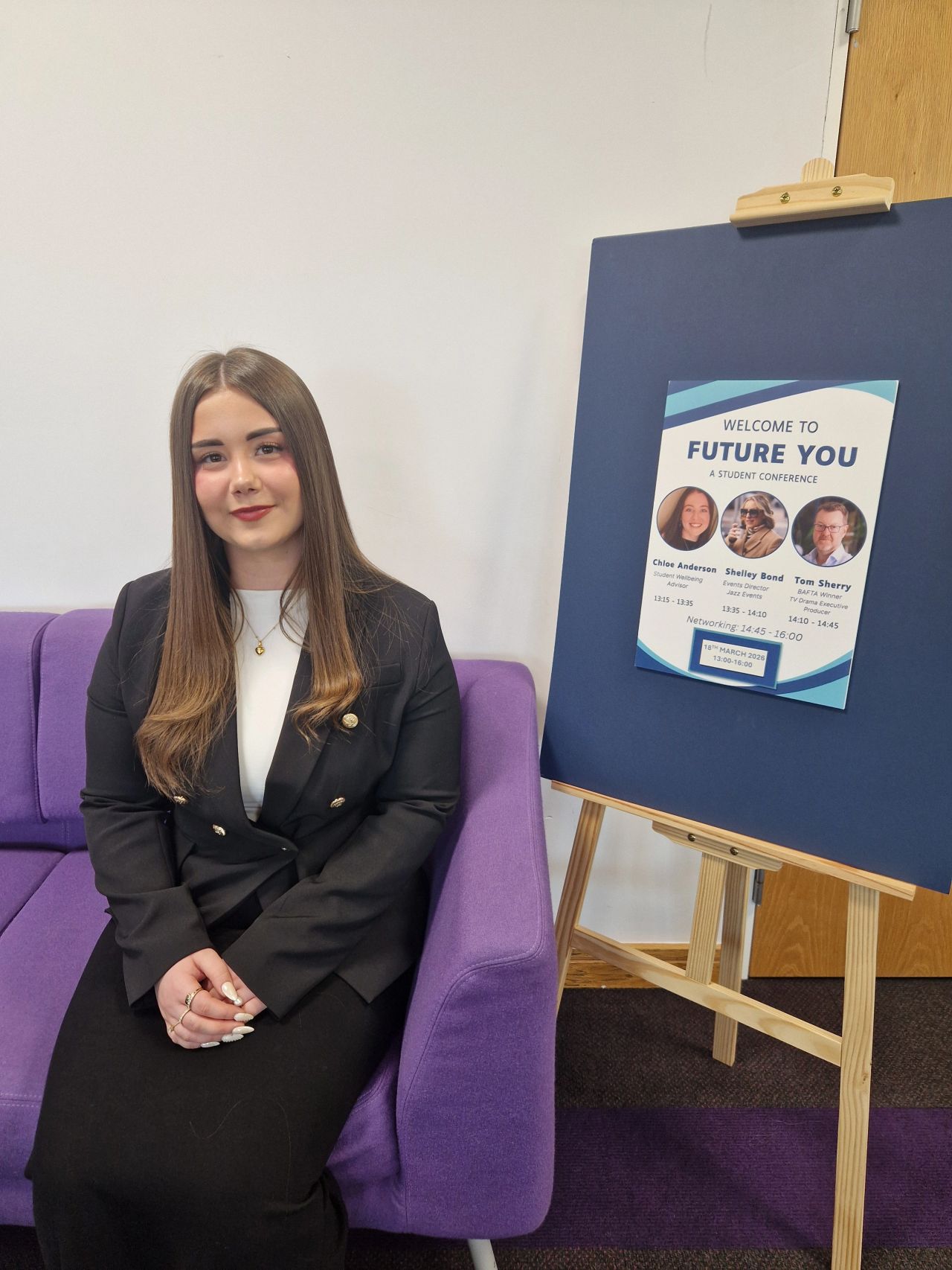 Abigail, a student, sat next to a poster for the Future You Student Conference