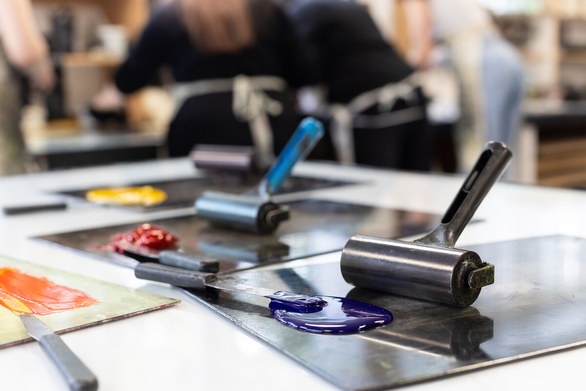 An art room with a table holding paint rollers, coloured paints on paper ready for use.