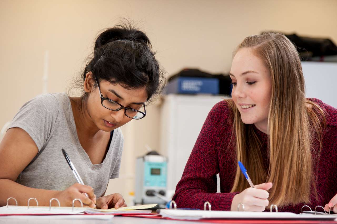 Two biology students writing notes and helping each other study.
