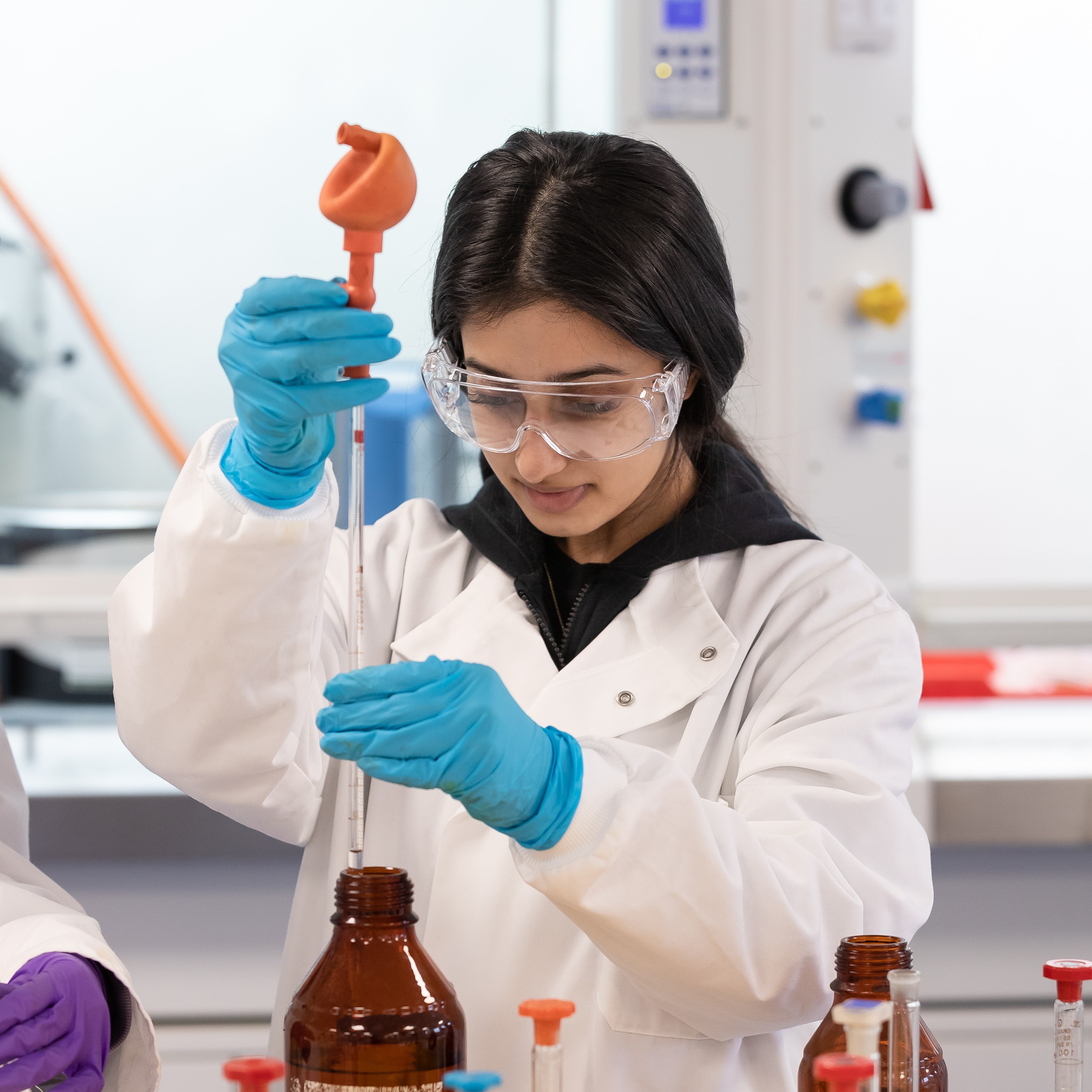 A student in a lab, holding a pipette.