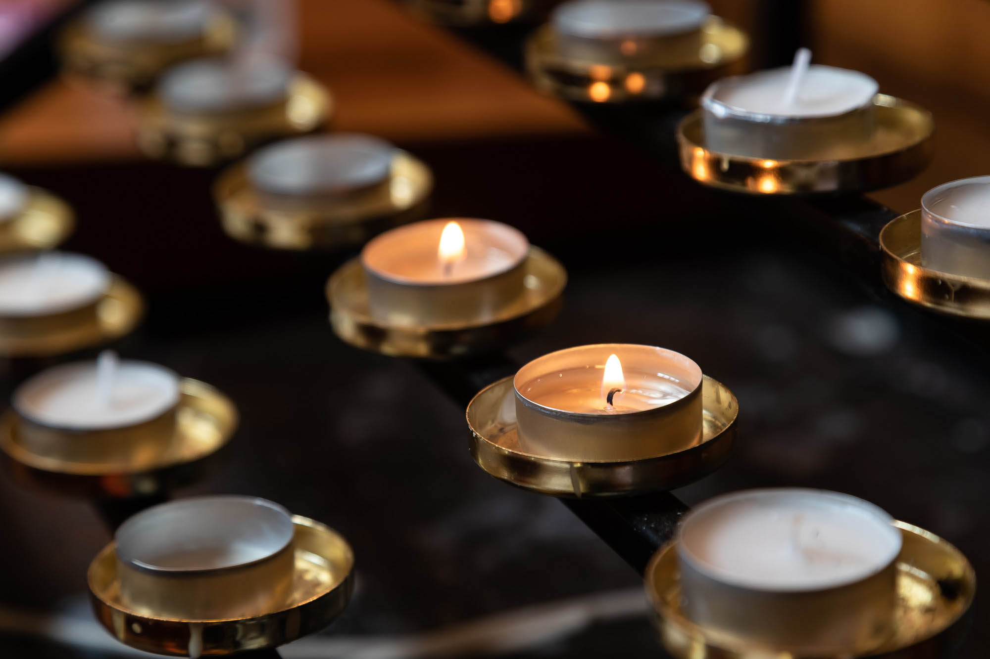 Close-up of lit and unlit candles in circular holders on a multi-tiered metal stand, creating a warm and tranquil ambiance.