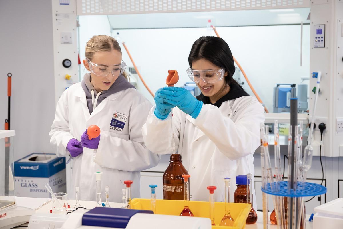 Chemical engineering Beng Hons student conducting process analysis on a digital tablet within an industrial laboratory setting, surrounded by stainless steel reactors, storage tanks, and process piping.