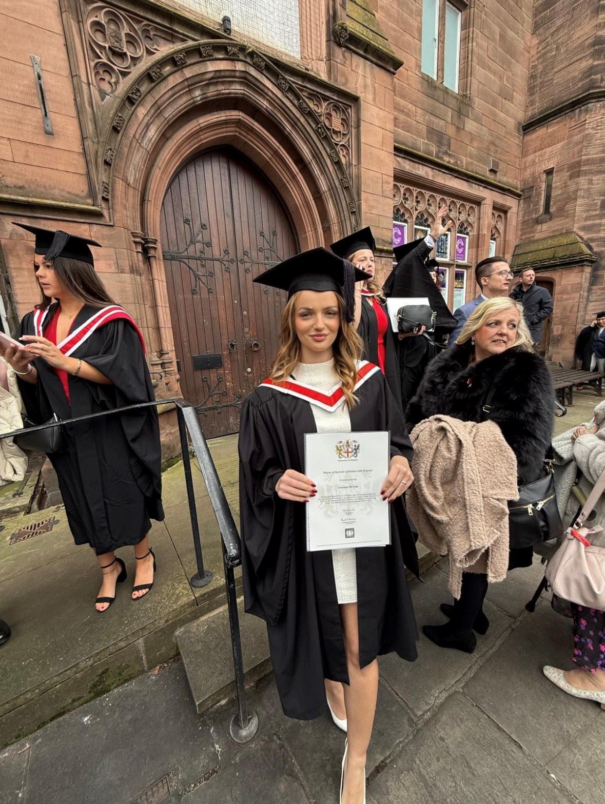 Courtney stood outside Chester Cathedral in her graduation cap and gown holding her graduation certificate
