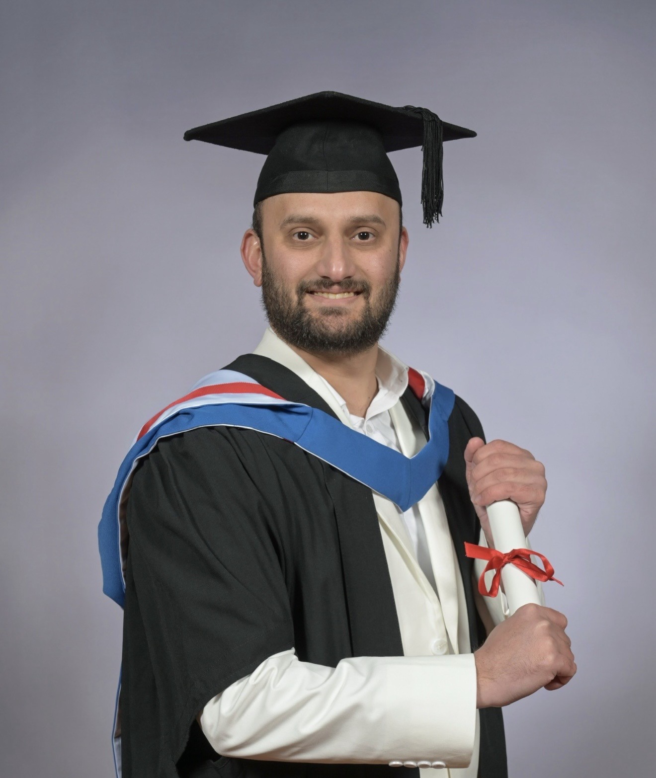 Fazale's official graduation image wearing a cap and gown and holding the degree scroll