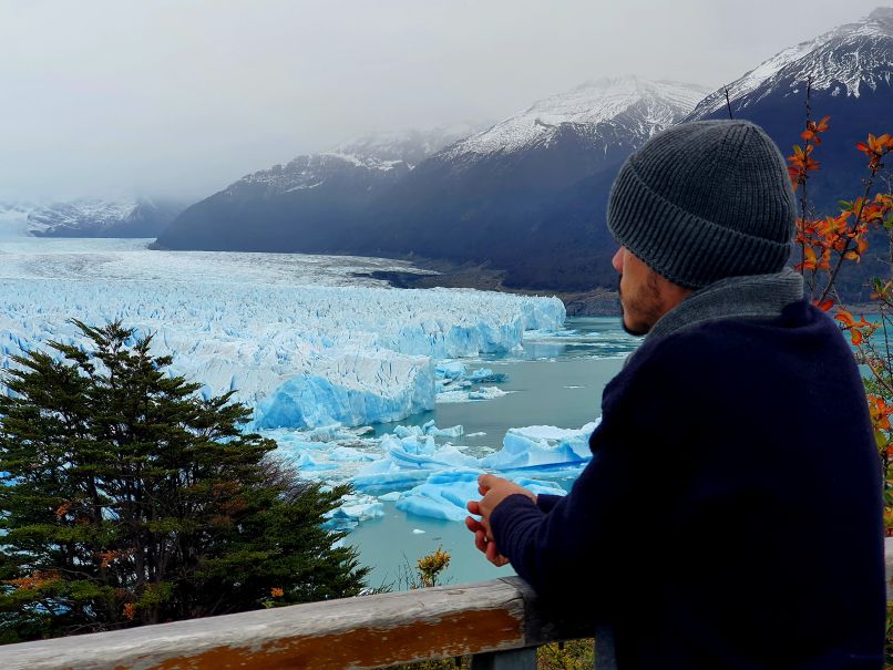 Luis looking out over a glacier lake with floating ice and snow-capped mountains in the background.