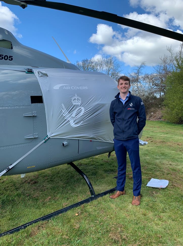 Scott stood in a field in front of a helicopter with an Air Covers product on it