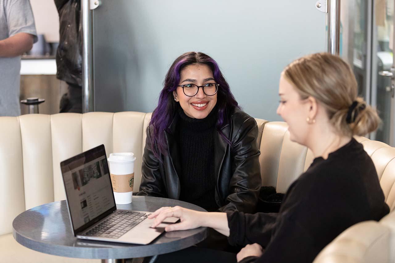 Two students discussing work on a laptop in a campus café, reflecting collaborative learning and engagement in Sociology with Criminology BSc Hons studies.