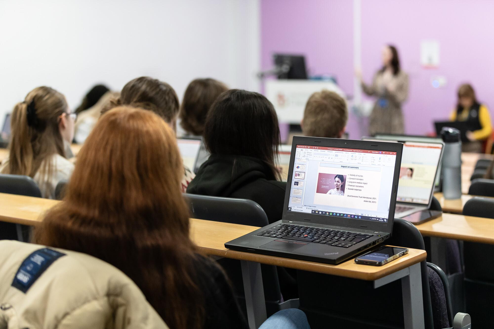 University students attending a Law with Criminal Justice LLB (Hons) lecture, taking notes and viewing legal presentation slides on laptops in a modern classroom.