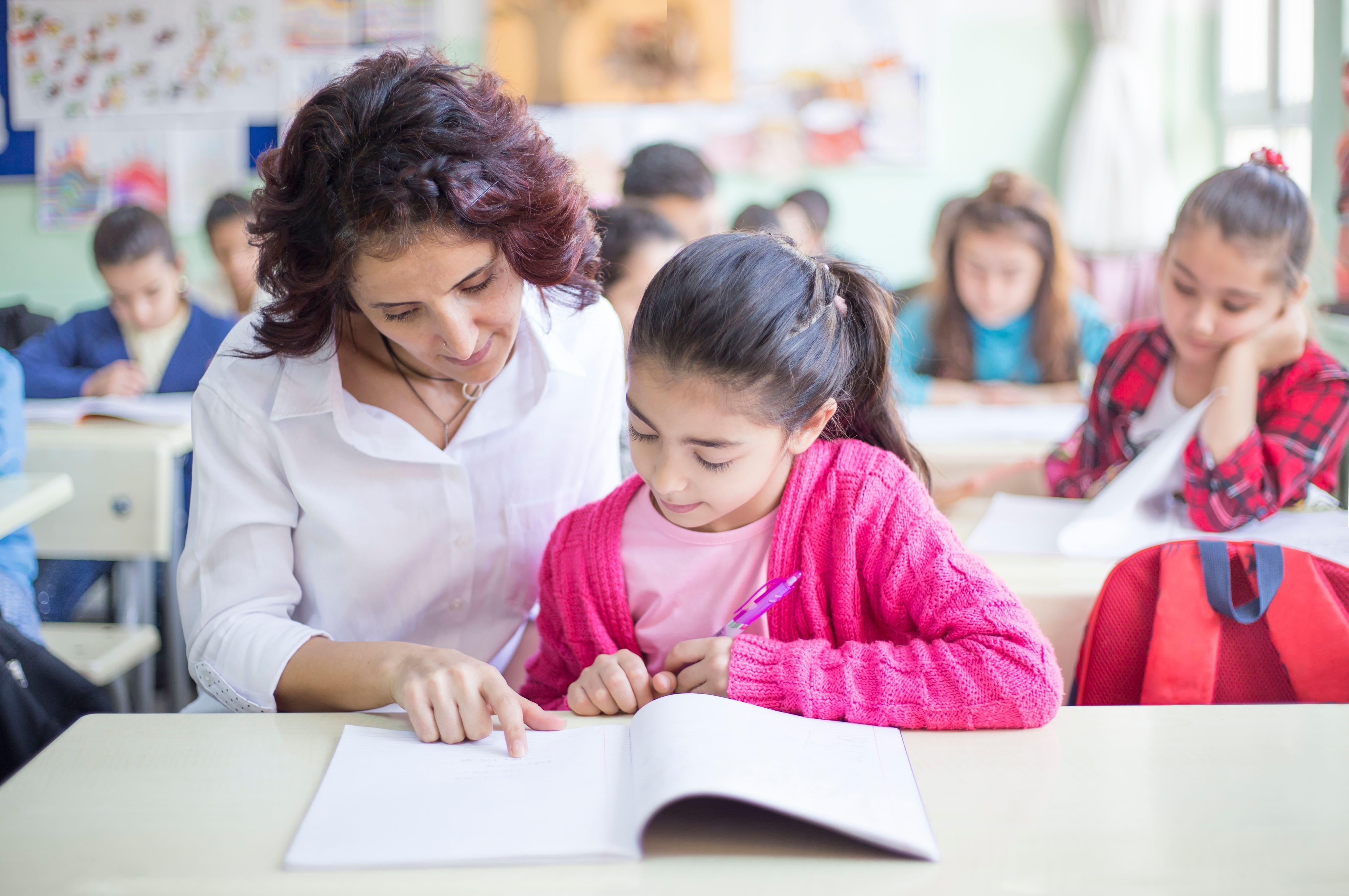Primary (5-11) School-Led PGCE with QTS trainee teacher supporting a pupil's learning in a primary school classroom, gaining practical teaching experience and Qualified Teacher Status through the University of Chester.