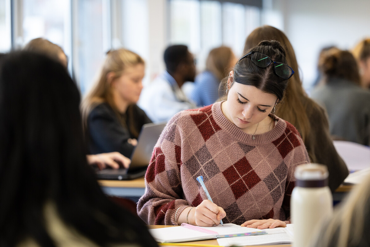A classroom during a teaching event, with a group of individuals seated at desks and engaging in note‑taking and laptop work