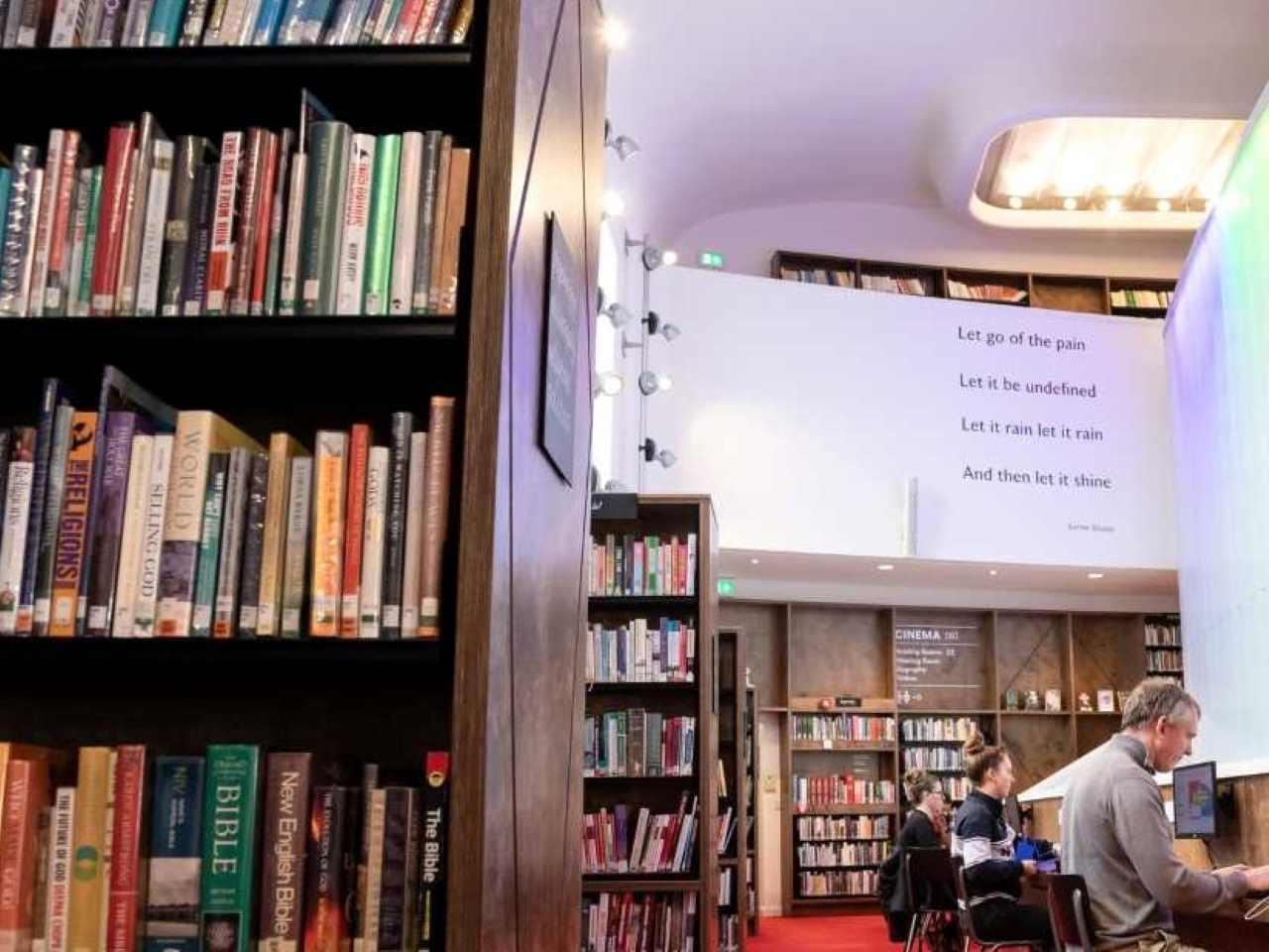 Students studying and writing in a modern university library surrounded by books, inspiring creativity for the Creative and Professional Writing BA (Hons) degree.