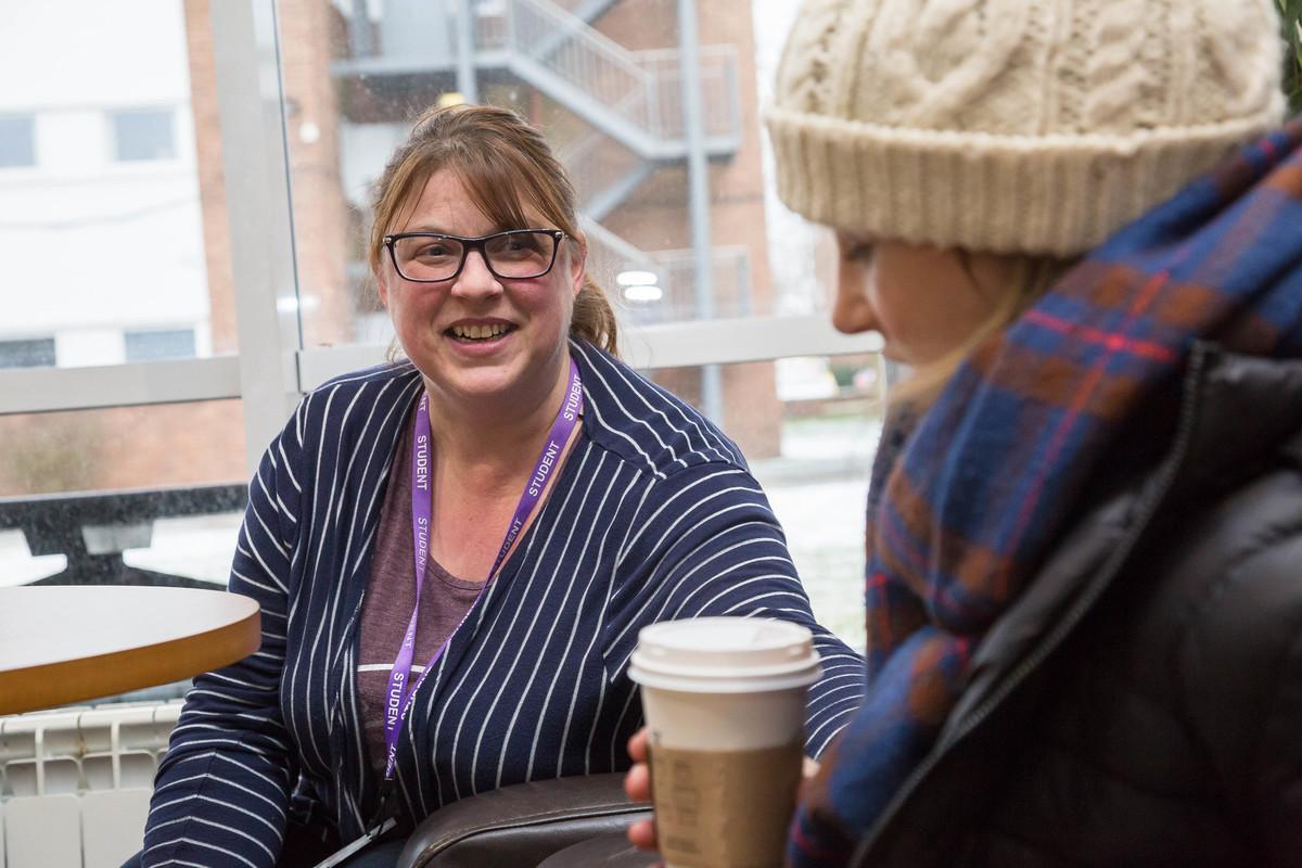 Two people in a campus setting having a supportive one-to-one conversation over coffee, illustrating communication skills, patient engagement and professional practice for Applied Mental Health Practice PGCert.