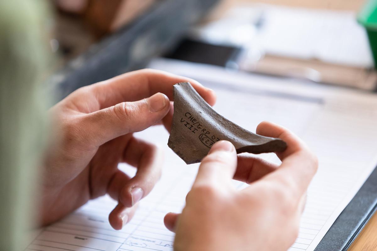 Archaeology and History student carefully examines a labelled pottery sherd during a hands-on workshop. The fragment, catalogued for research, illustrates the practical skills students develop on the Archaeology and History BA (Hons) course.