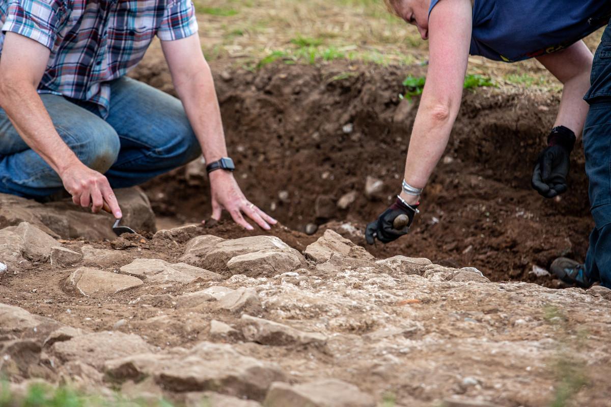 Archaeology students carefully excavating a historic site with hand tools, revealing stone structures and artefacts, demonstrating fieldwork techniques, excavation methods and research skills for Archaeology MRes.