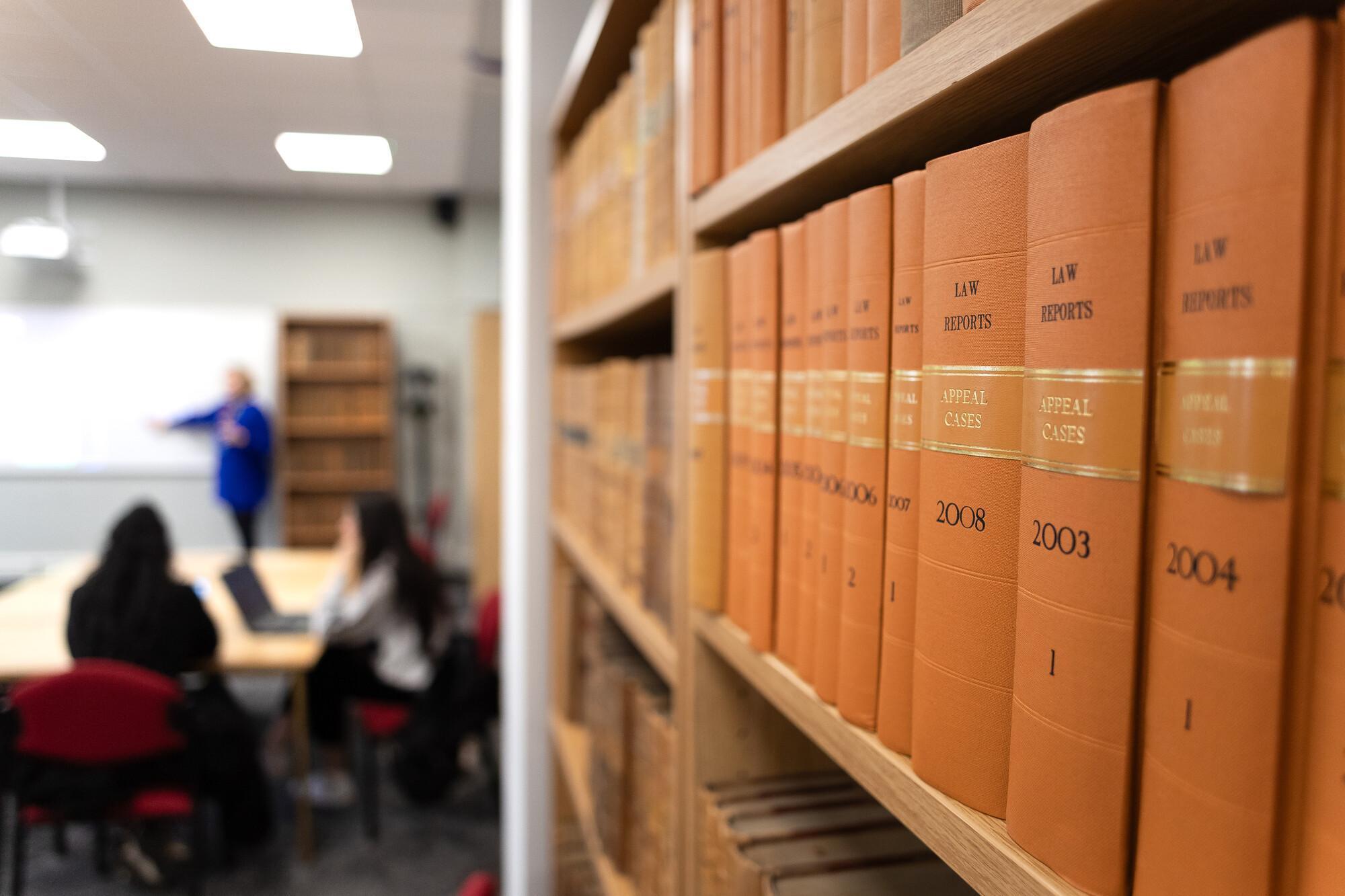 Law students learning in a university classroom with shelves of legal case books, representing the Law with Business and Commerce LLB degree.