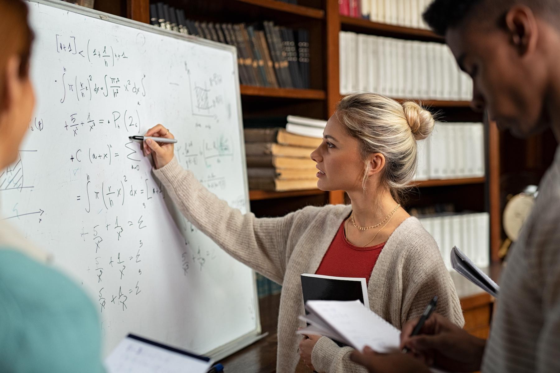 Mathematics BSc students collaborating to solve advanced equations on a whiteboard during a university math lecture in a library study environment.