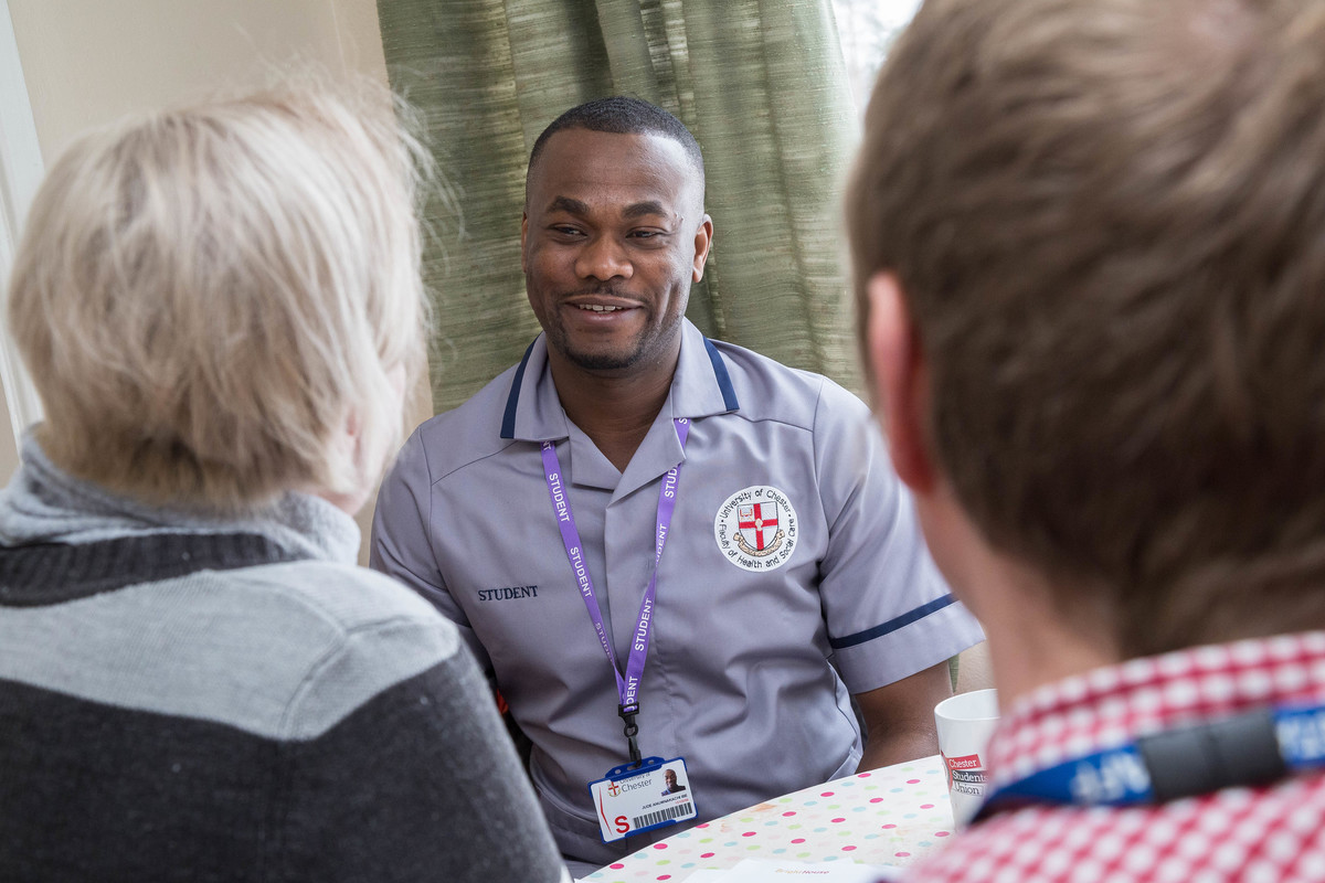 Nursing degree student smiling and talking with two people, showing supportive and compassionate care.