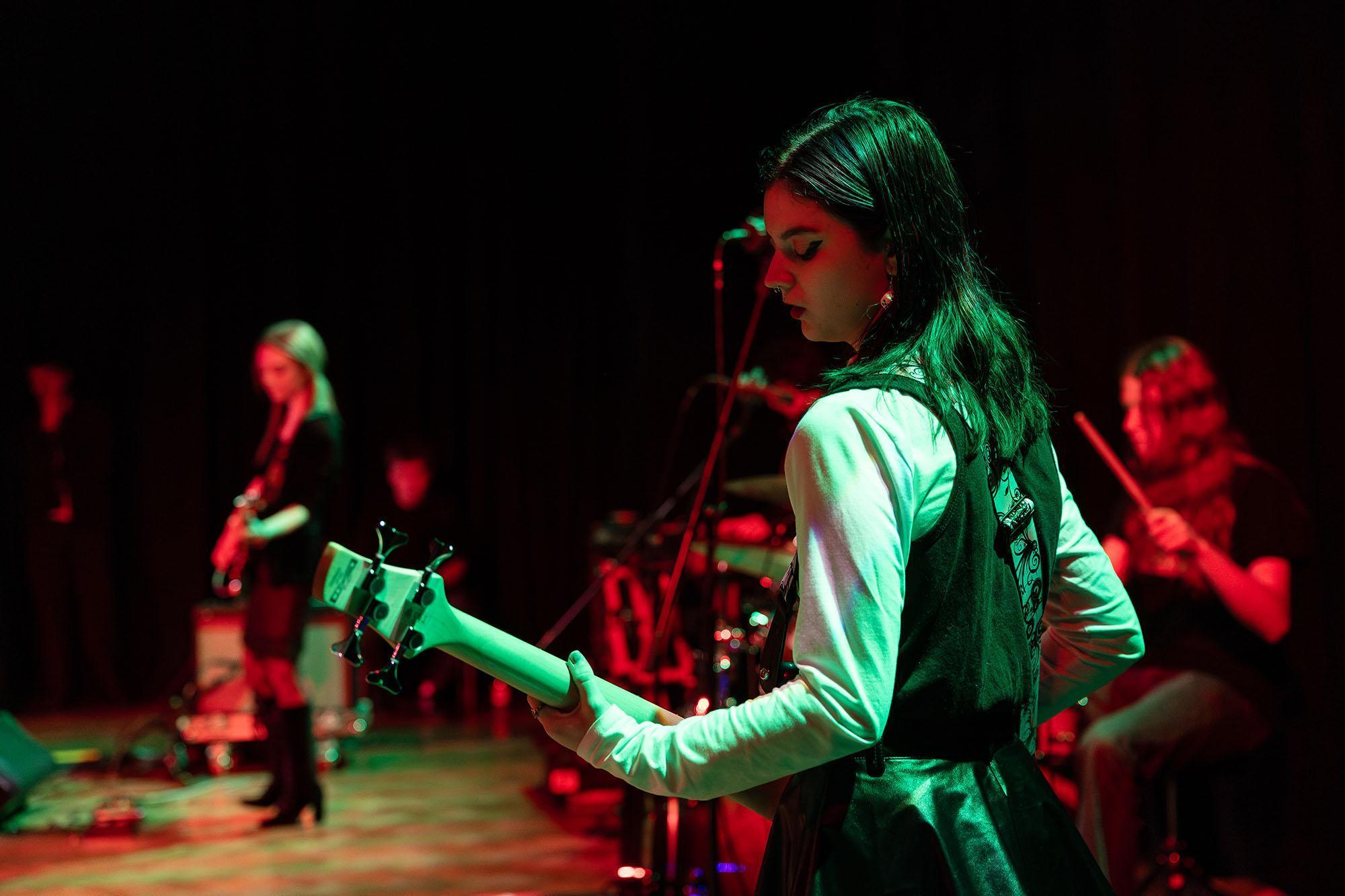 Students performing live on stage with electric guitars and drums under vibrant red and green lighting, showcasing practical skills developed on the Popular Music Performance BA (Hons) course.