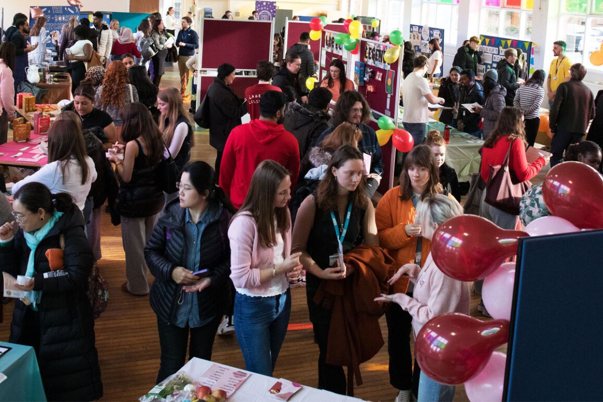Students walking around a busy hallroom at a number of stalls in last year's nutrition fair. There are partitions with banners and balloons.