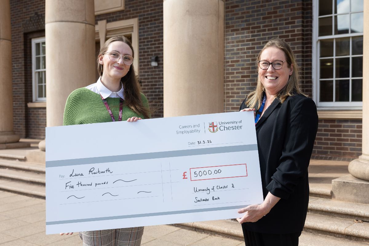 Two women facing the camera, smiling, holding a giant £5,000 cheque. On the left is student Luna, on the right is Angela Standish.