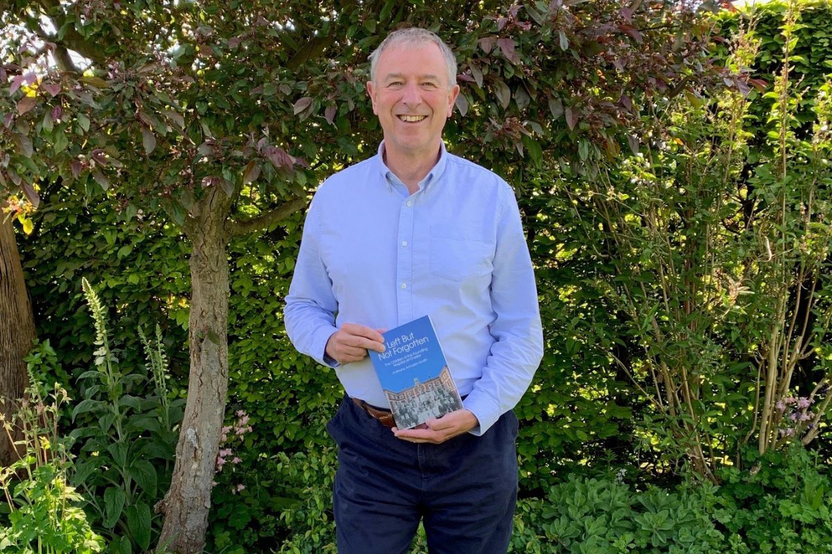 A man, smiling while looking at the camera, presenting a book being held in his hands.