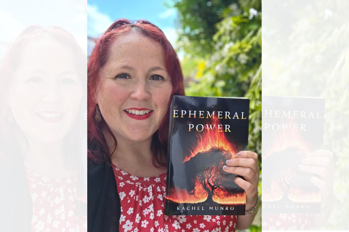 Rachel Munro smiling at the camera while holding a copy of her book, titled Ephemeral Power. The book cover is mostly in silhouette, with flames rising from a tree.