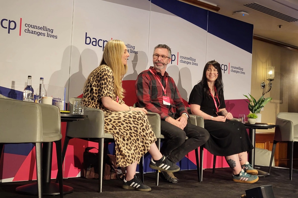 Two women either side of a man, all sat down, in discussion on a stage. In the background is the BACP logo.