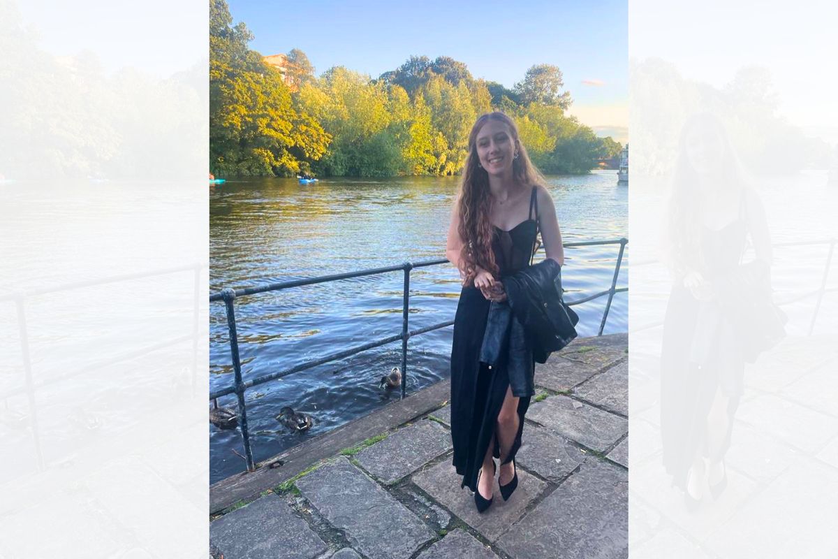 A student standing and smiling at the camera. In the background is a river and trees.