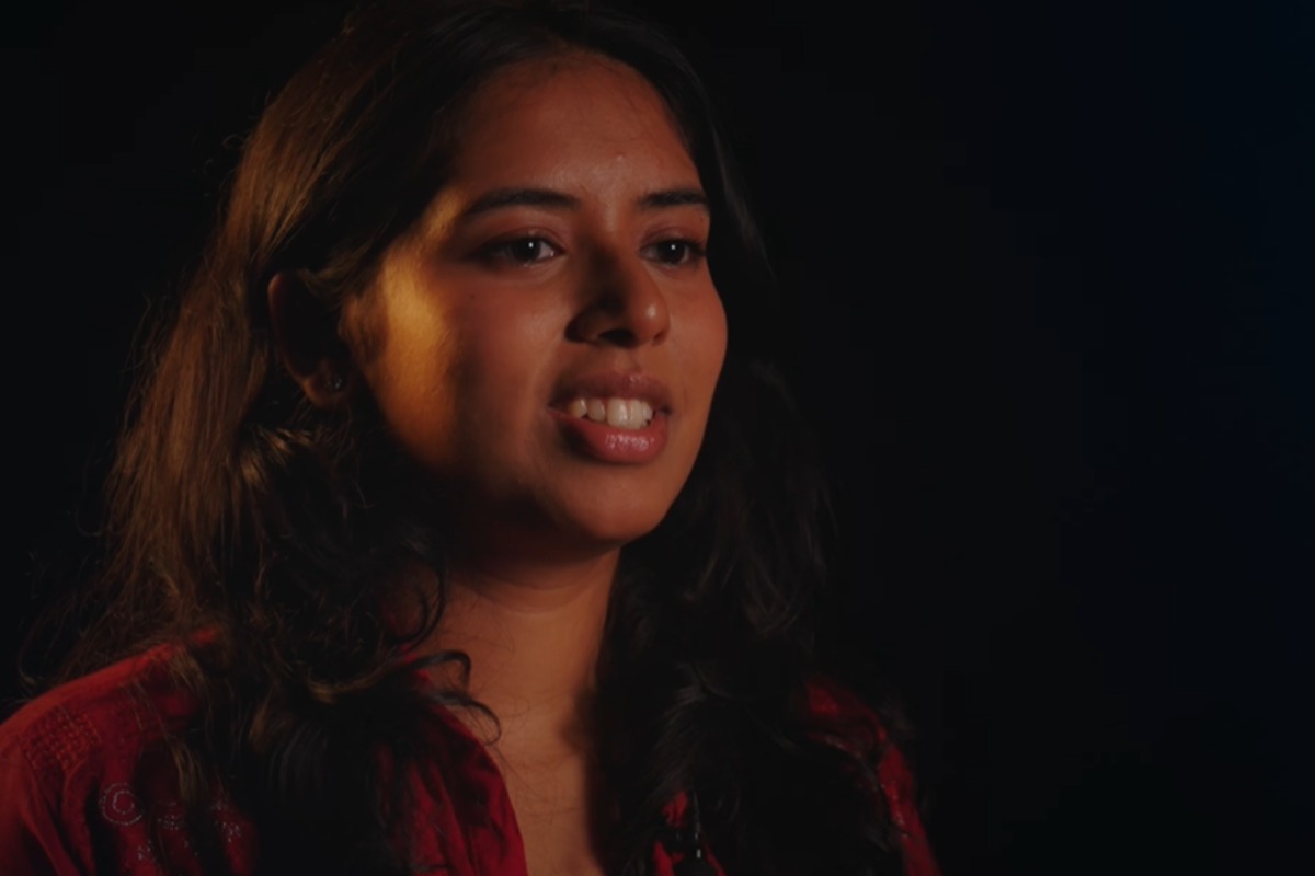A young woman speaking against a black background.