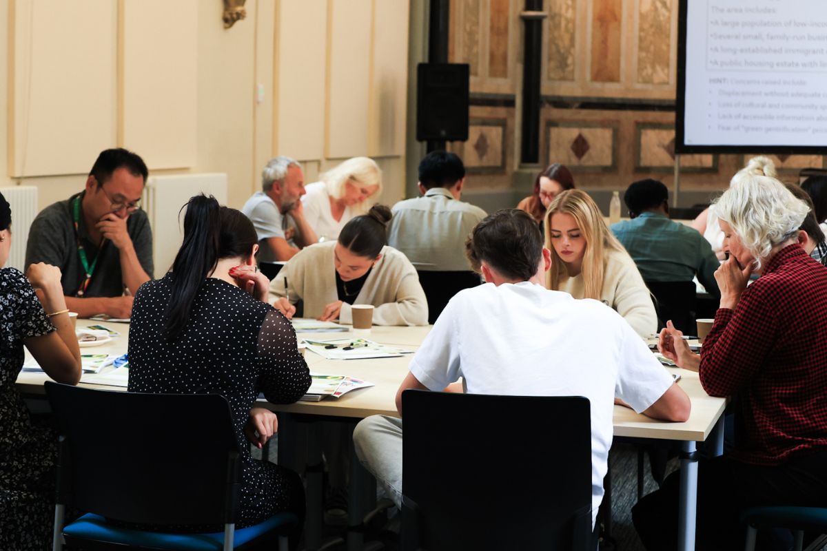 Two groups of people sitting around two tables, writing notes.
