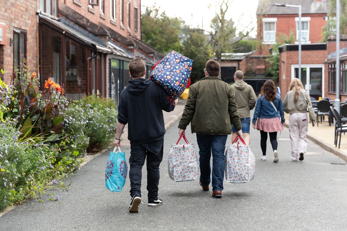 Two students walking away from the camera, carrying a number of big bags.