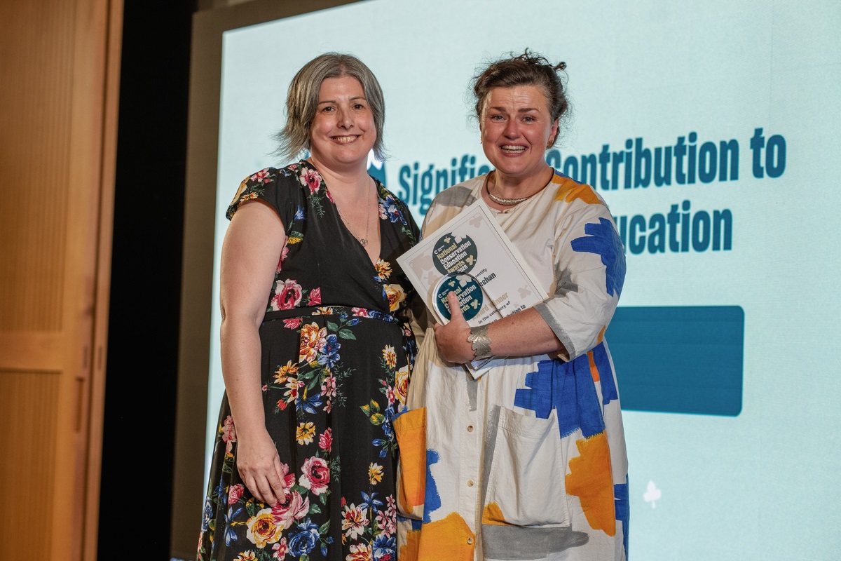 Una Meehan, pictured right with an award, smiling at the camera. The woman on the left of her is Charlotte Smith, alos smiling and looking at the camera.