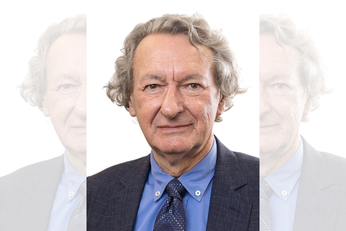 A head-and-shoulders picture of a man in a blue shirt and a tie facing the camera, in front of a white, blank background.
