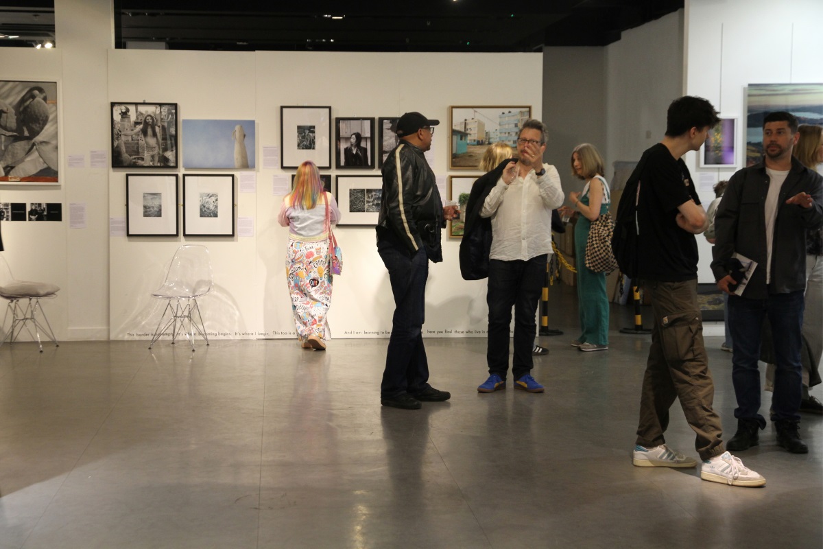 A group of people in a gallery, looking at framed photos on the walls.