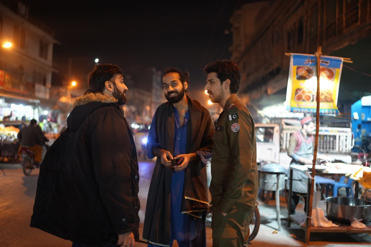 Three men in discussion with each other on a street in night-time.