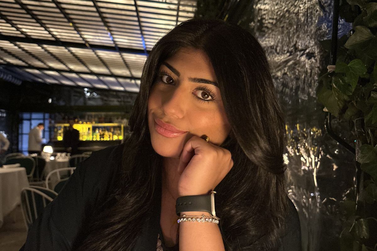 A woman sat down with her face resting on her left hand, looking at the camera, in a sheltered bar.