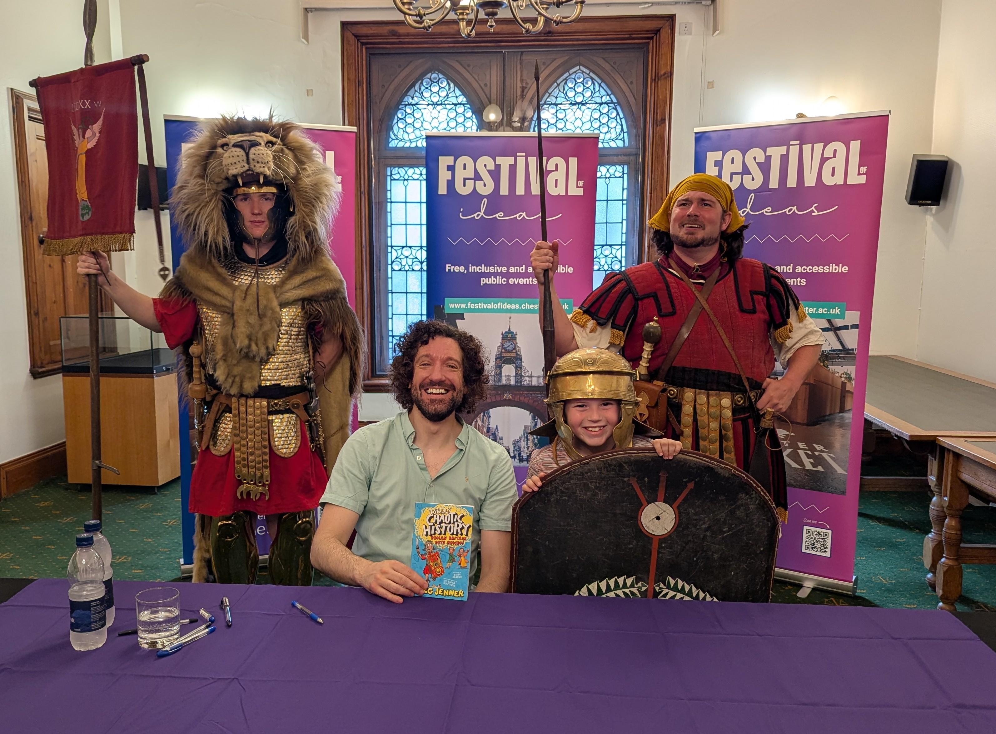 Greg Jenner signing a book, flanked by Roman soldiers from Chester Roman Tours.