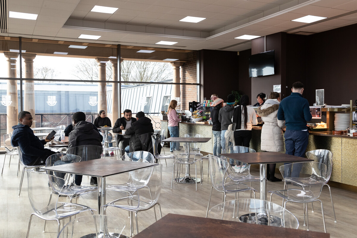 Busy university café with modern seating, large windows, and people sitting and queuing at the counter.
