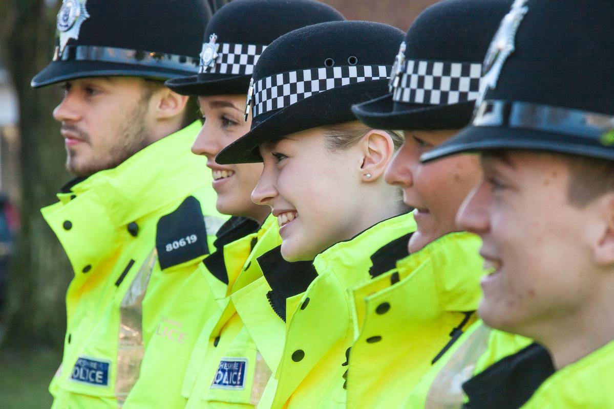Group of smiling police officers in bright yellow jackets and traditional black hats during training, representing Professional Policing BSc (Hons) students.