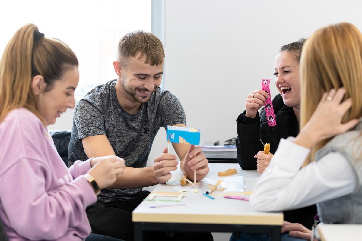 Group of Social Work BA (Hons) students collaborating in a classroom activity, smiling and working together on a hands-on project, demonstrating teamwork, communication, and practical learning skills.