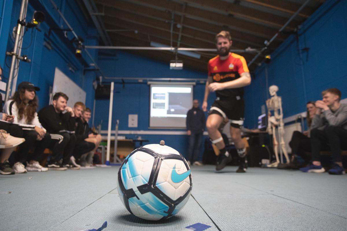 Sport and Exercise Sciences students analysing biomechanics as a footballer performs a movement test in a sports lab.
