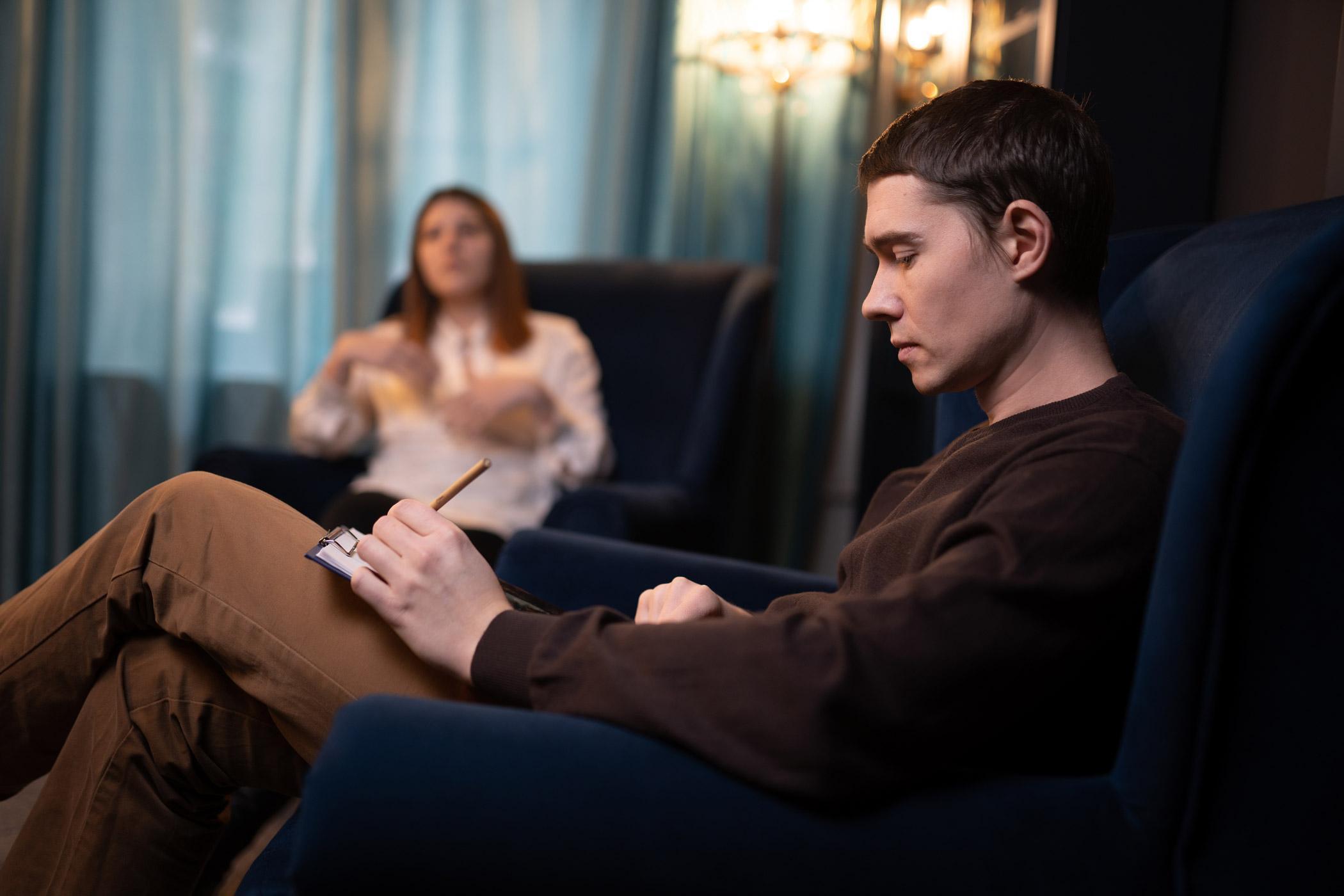 A counsellor takes notes while listening to a person during a session, illustrating skills taught in the PGCert in Trauma Psychology, Online Masters in Trauma Psychology, and Trauma Therapy Courses for the Psychological Trauma (Online Delivery) PGCert.