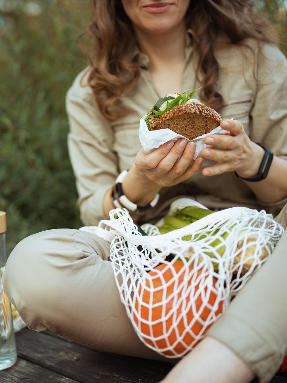 Elegant female in overall eating while sitting outdoors in city.