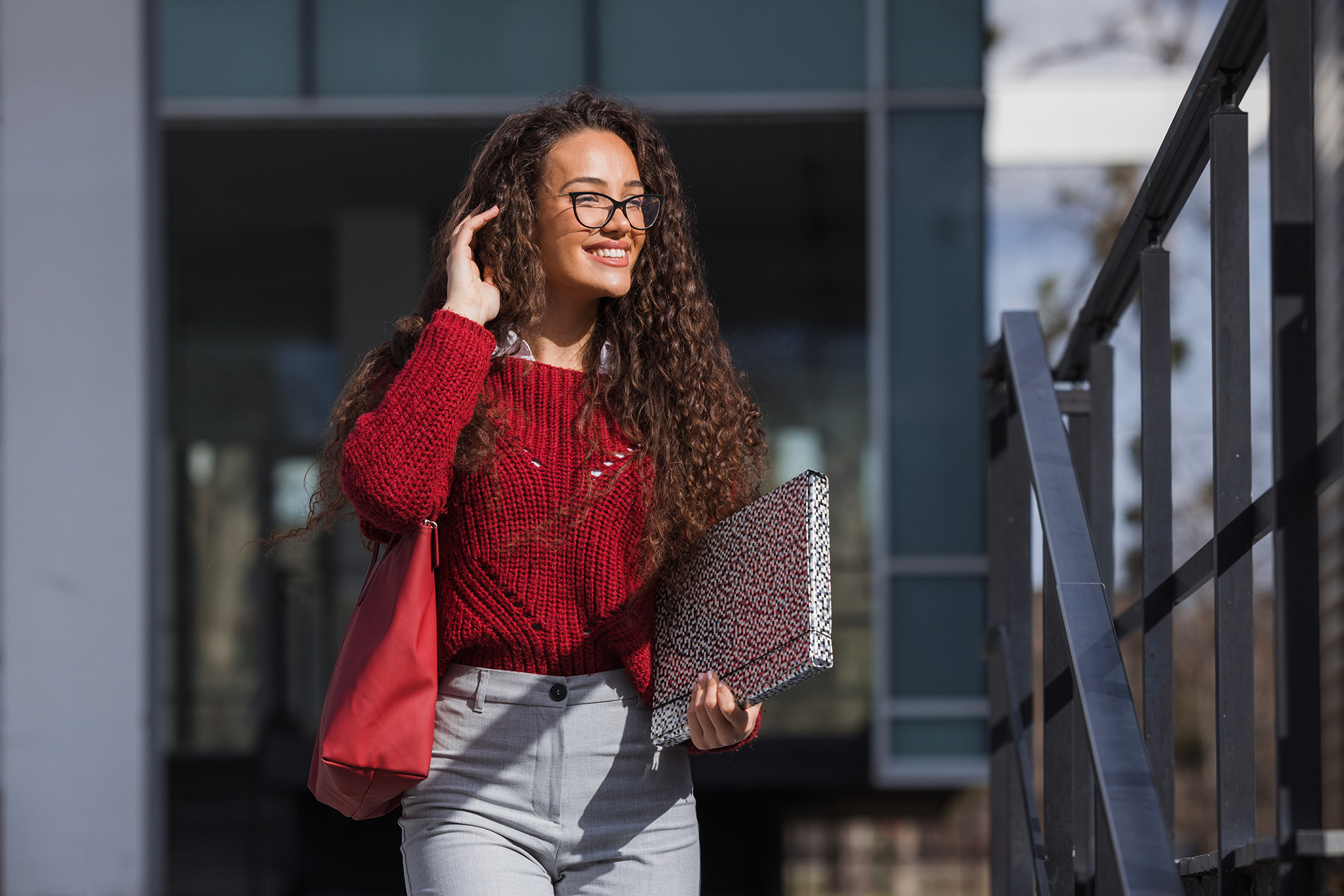 Female student in red top with big smile and one hand in hair while holding a folder with the other.