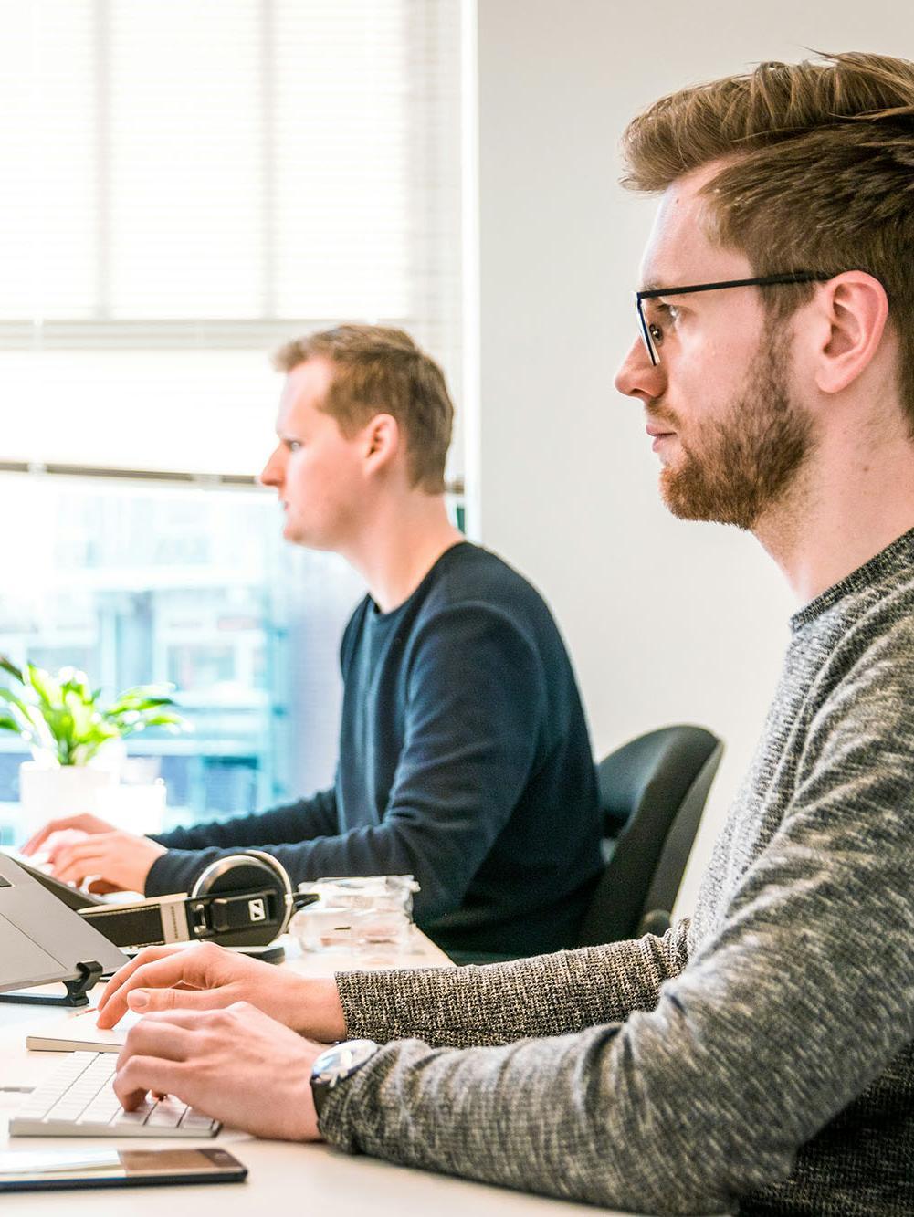 Man sitting on chair wearing gray crew-neck long-sleeved shirt using Apple Magic Keyboard.